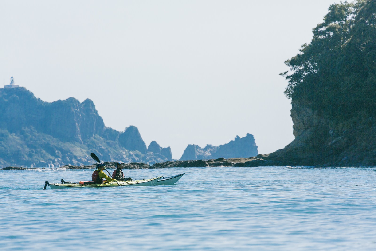 栄松ビーチの海でシーカヤックを漕ぐ人と背景の岩場