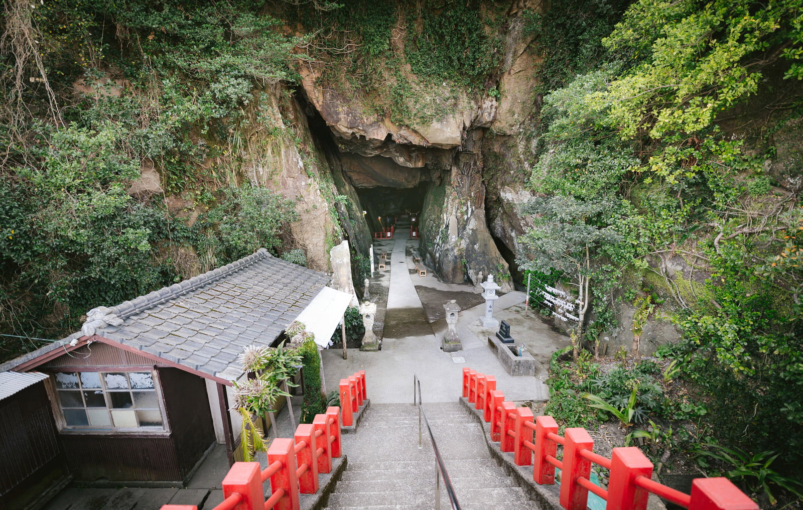 緑に囲まれた洞窟状の岩場にある祇園神社の赤い手すりが設置された参道