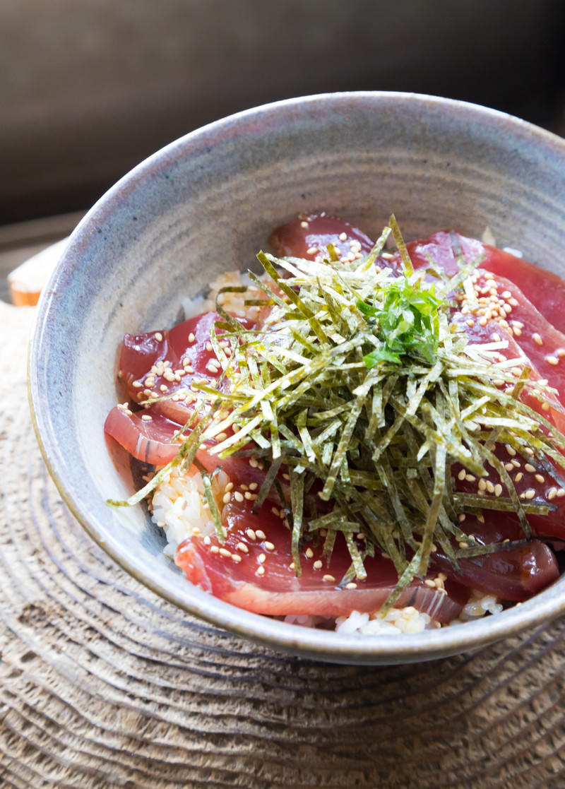 白いどんぶりに盛られた鰹めし。切り身、ゴマ、青ねぎがのってい