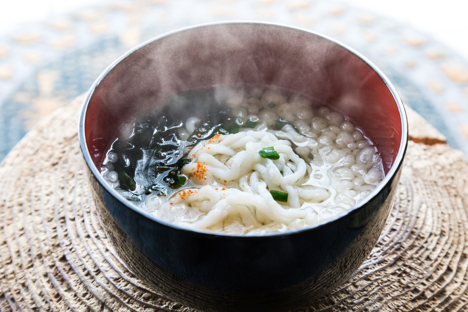 黒いお椀に盛られた湯気の立つ魚うどん。白い太麺に海苔とネギが乗っている