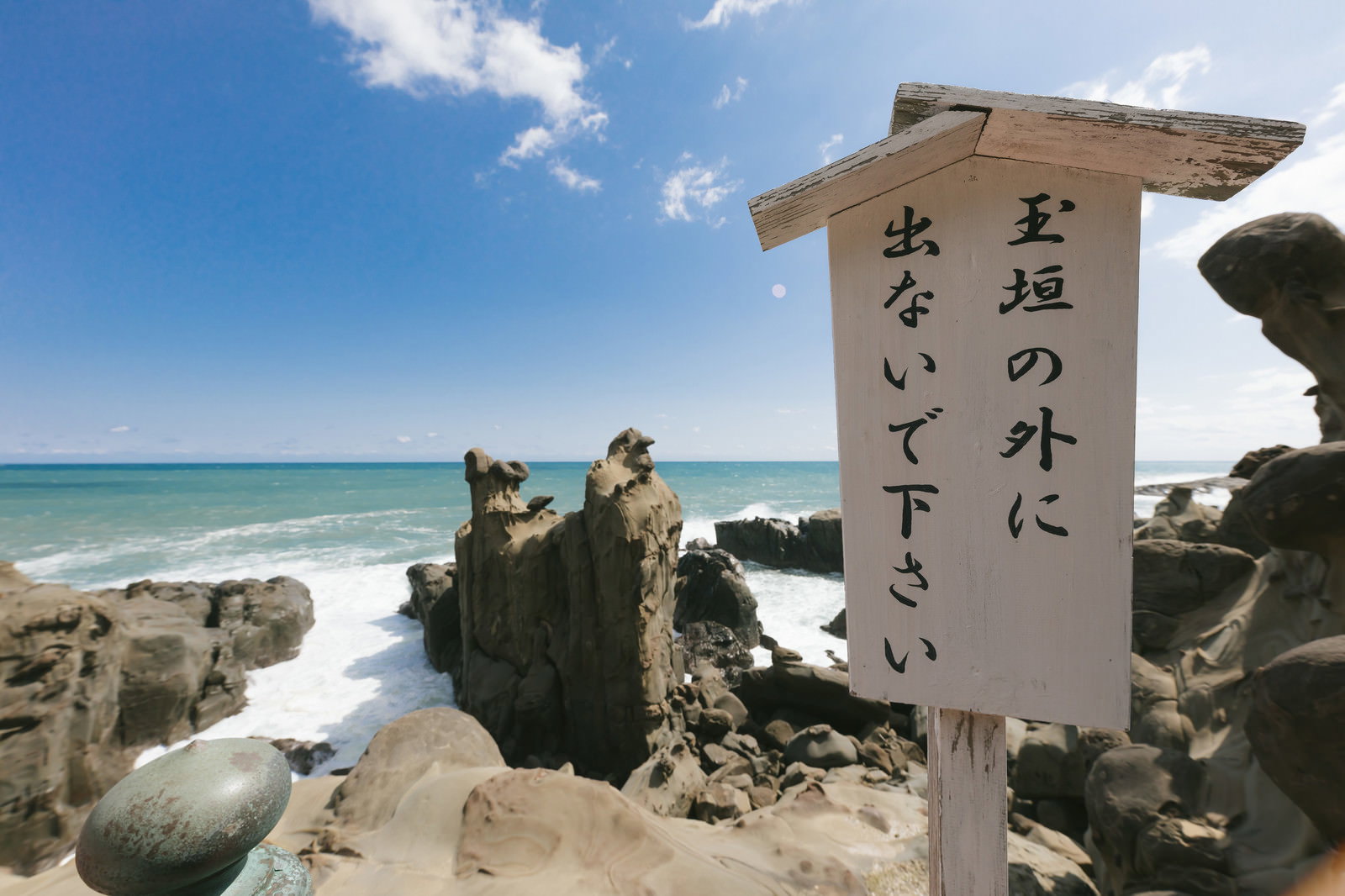 海に面した断崖に立つ白い警告板と岩場、青い海の風景