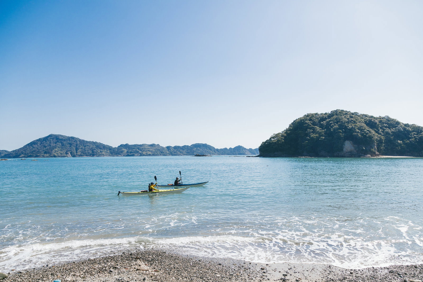 栄松ビーチの青い海でシーカヤックを楽しむ2人と美しい海岸線