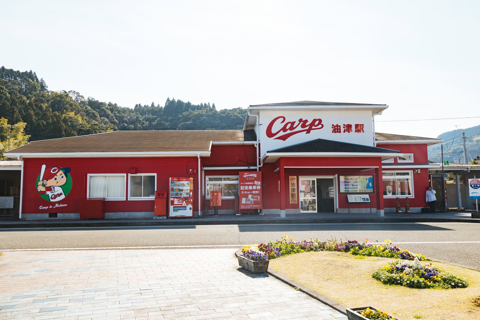 赤いカープカラーの油津駅舎と駅前広場の風景