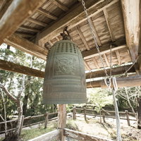 飫肥城跡に吊り下げられた青銅色の鐘と木造建築の写真