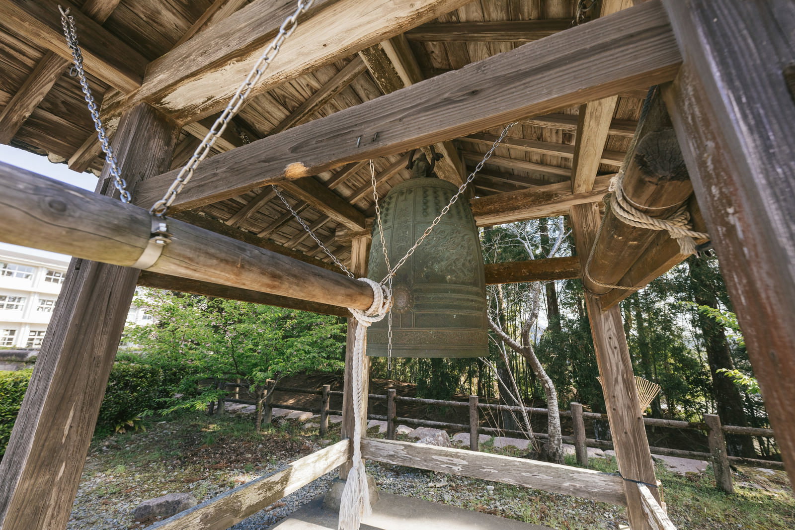 飫肥城の木造鐘楼に吊り下げられた古い鐘と緑の風景