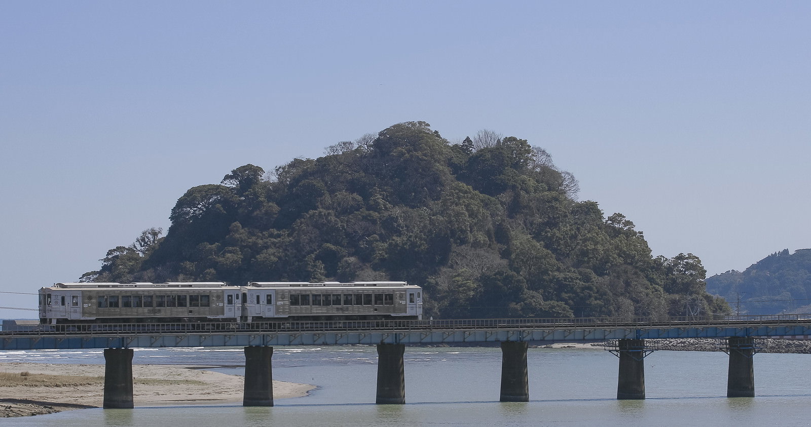 虚空蔵島の緑を背景に、橋の上を走る白い観光列車と海岸の風景