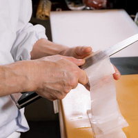 黄色いまな板で大根を桂剥きする寿司職人の手元の写真