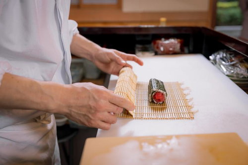 巻き簾の上に置かれた鉄火巻を寿司職人が仕上げている調理風景