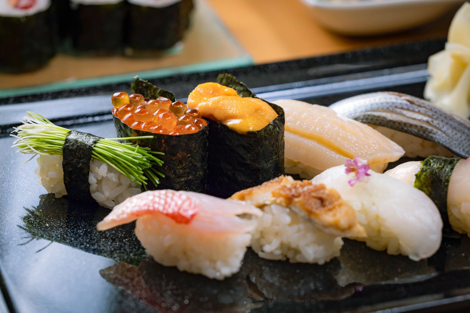 黒い皿に盛られたうに、いくら、ホタテ、マグロなど様々な握り寿司