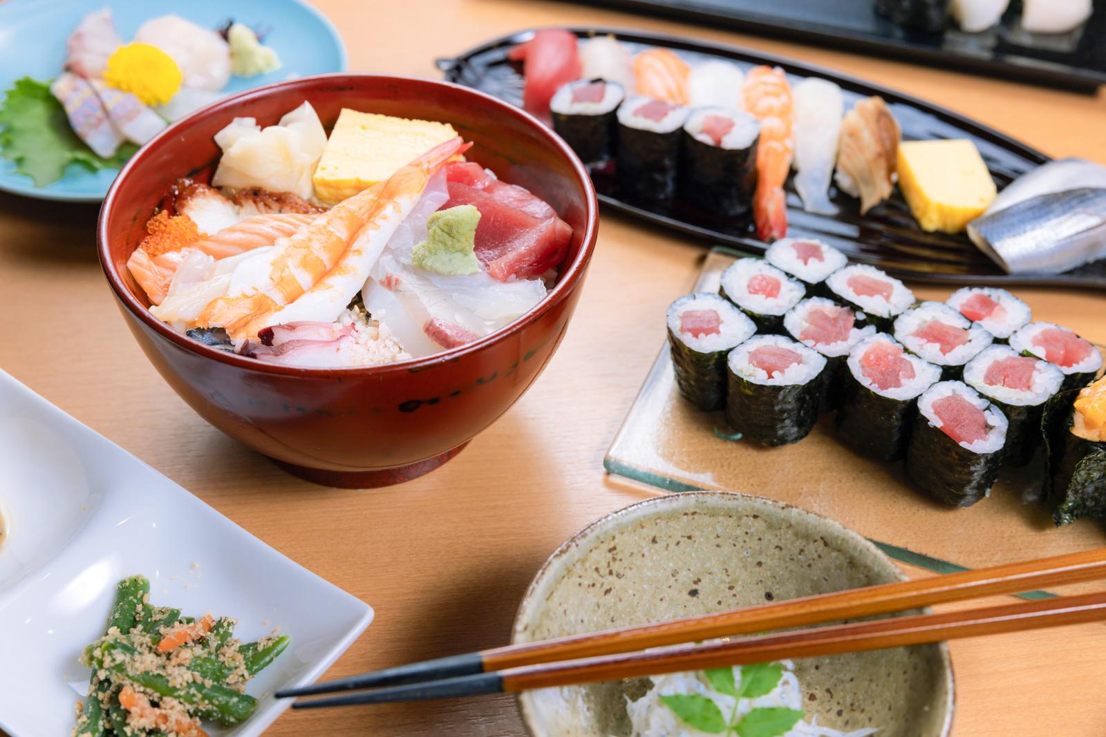 赤い椀の海鮮丼と黒い皿の握り寿司・巻き寿司が食卓に並ぶ