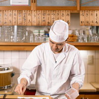 木製カウンター越しに下ごしらえをする寿司職人の写真