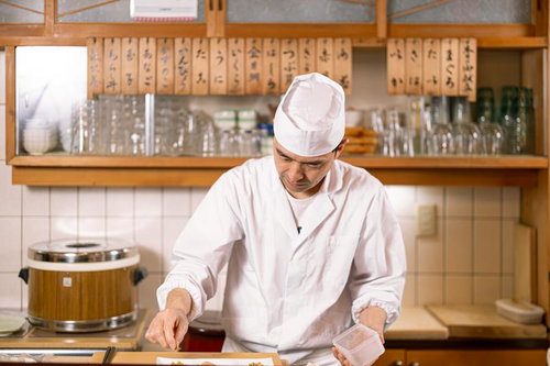 木製カウンター越しに下ごしらえをする寿司職人