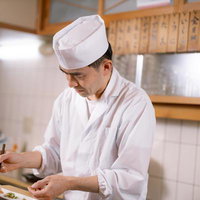 寿司職人がカウンター越しに箸を使って盛り付ける調理の写真