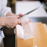 寿司職人が切れ味のよい包丁で大根を薄く桂剥きする様子の写真