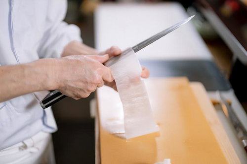 寿司職人が切れ味のよい包丁で大根を薄く桂剥きする様子