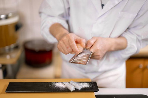 寿司職人がおろし金で刺身に岩塩をすりおろす