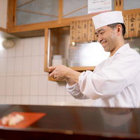 笑顔で寿司を握る寿司職人のカウンター仕事風景の写真