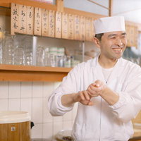 にこやかな笑顔で握り寿司を握る寿司職人の店主の写真