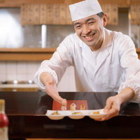 人柄あふれる寿司職人がカウンターで握り寿司を提供するの写真