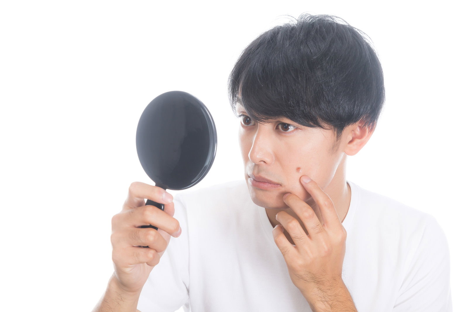 手鏡を持って頬のニキビを確認している白いシャツの男性［モデル：完伍］