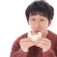 肉まんを食べて感動する赤いセーターの男性の写真