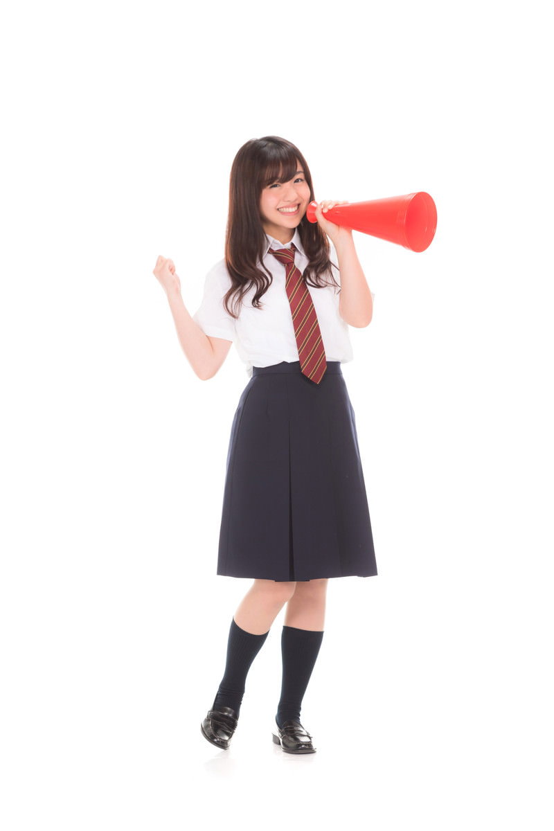 赤いメガホンを持って片手を上げ応援する制服姿の女子高生［モデル：河村友歌］
