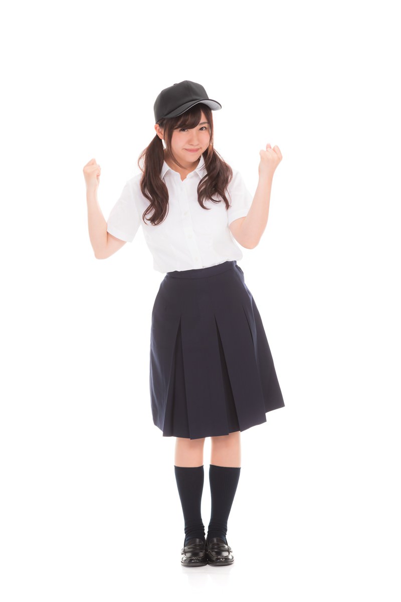黒キャップを被り、白シャツと紺スカートの制服姿で両腕を上げてガッツポーズをする女子高生［モデル：河村友歌］
