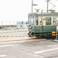 鎌倉高校前駅の踏切を走行する江ノ電、黄黒のバーが目印の写真