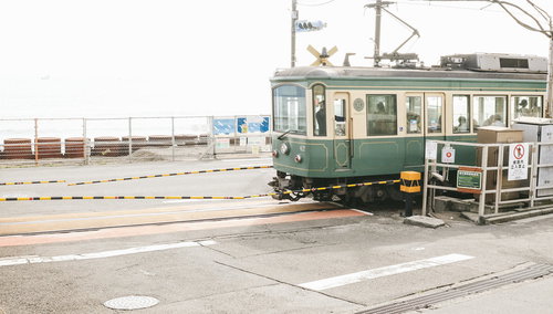 鎌倉高校前駅の踏切を走行する江ノ電、黄黒のバーが目印