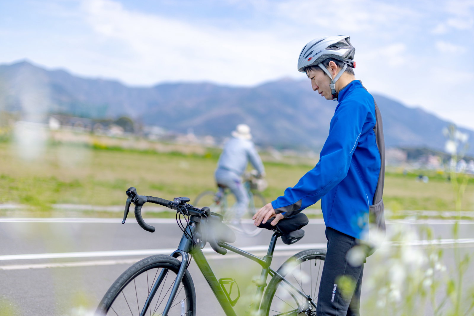 青いサイクリングウェアとヘルメットを着用した男性が自転車道でロードバイクをチェックしている［モデル：モデルリリース］