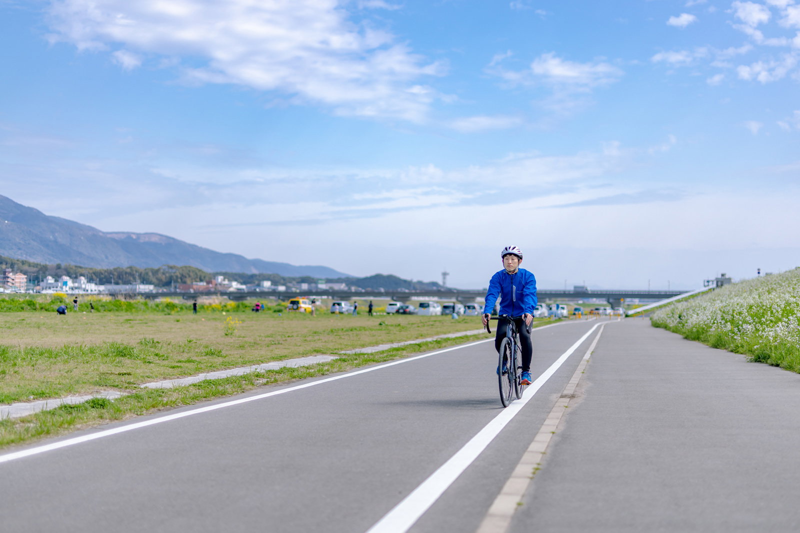 青空の下、直方北九州自転車道をロードバイクで走る男性の後ろ姿［モデル：モデルリリース］