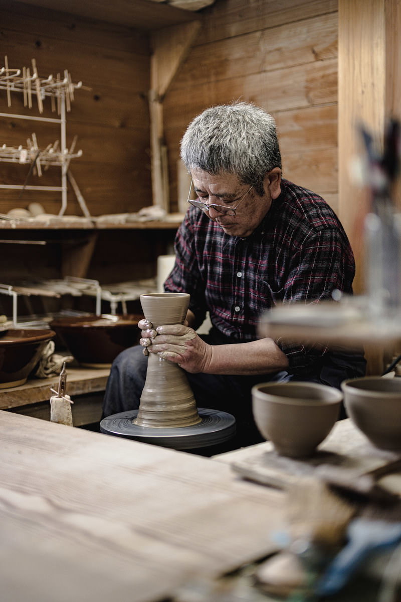 工房でろくろを回しながら陶器を作る陶芸家の男性［モデル：モデルリリース］