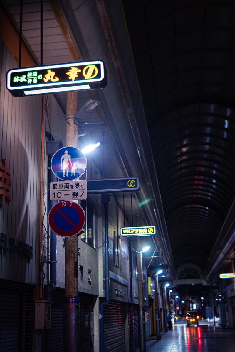 シャッターが閉まった夜のアーケード商店街、看板の明かりが通りを照らしている
