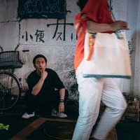 薄暗い路地で通りがかる女性を眺める男性の後ろ姿の写真