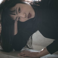 静かな笑みをこぼしながらポージングする黒髪の女性の写真