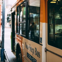 停留所に停車する緑とベージュのノンステップバスの写真