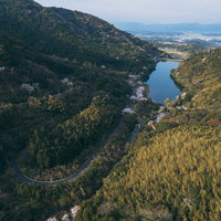 遠景のダム湖と峠道を俯瞰した春景色、内ヶ磯ダムのドローン空撮の写真