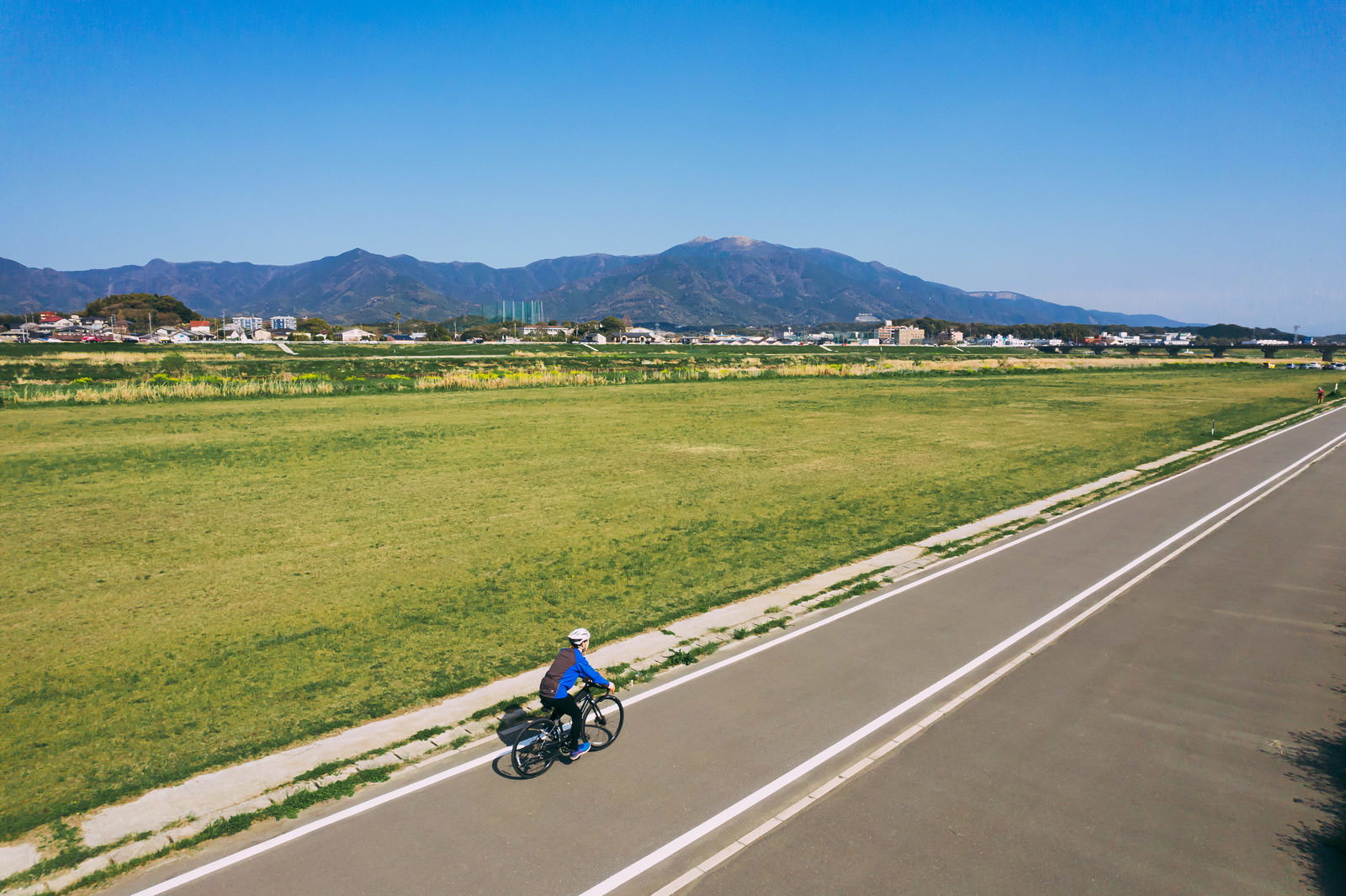 青空と山並みを背景にサイクリングロードを走るロードバイク
