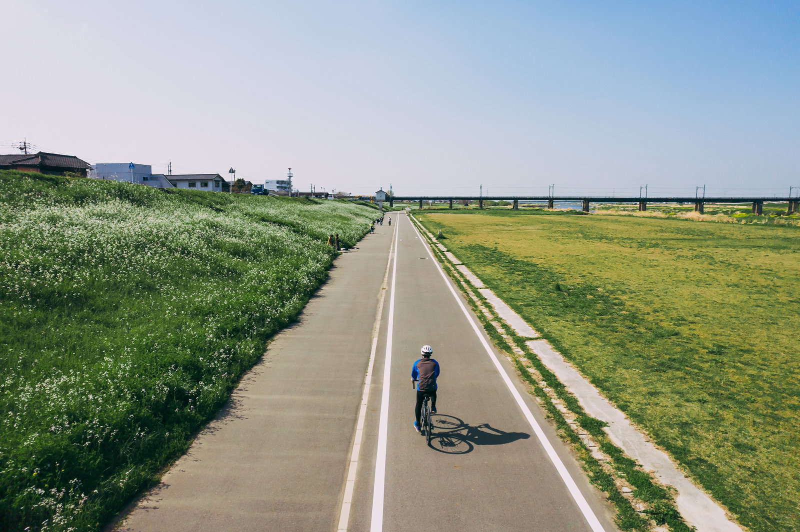 河川敷の自転車道を走るサイクリストと青空が広がる風景