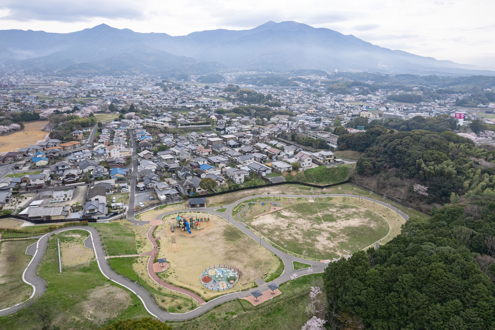 直方市の中央公園と周辺住宅地の空撮写真、緑の公園と山並み