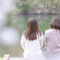 川沿いの桜並木で花見を楽しむ女性たちの後ろ姿の写真