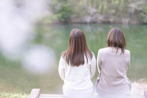 川沿いの桜並木で花見を楽しむ女性たちの後ろ姿