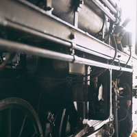 光を浴びる蒸気機関車の足回りと駆動輪、複雑に組み合わさったロッド機構の写真