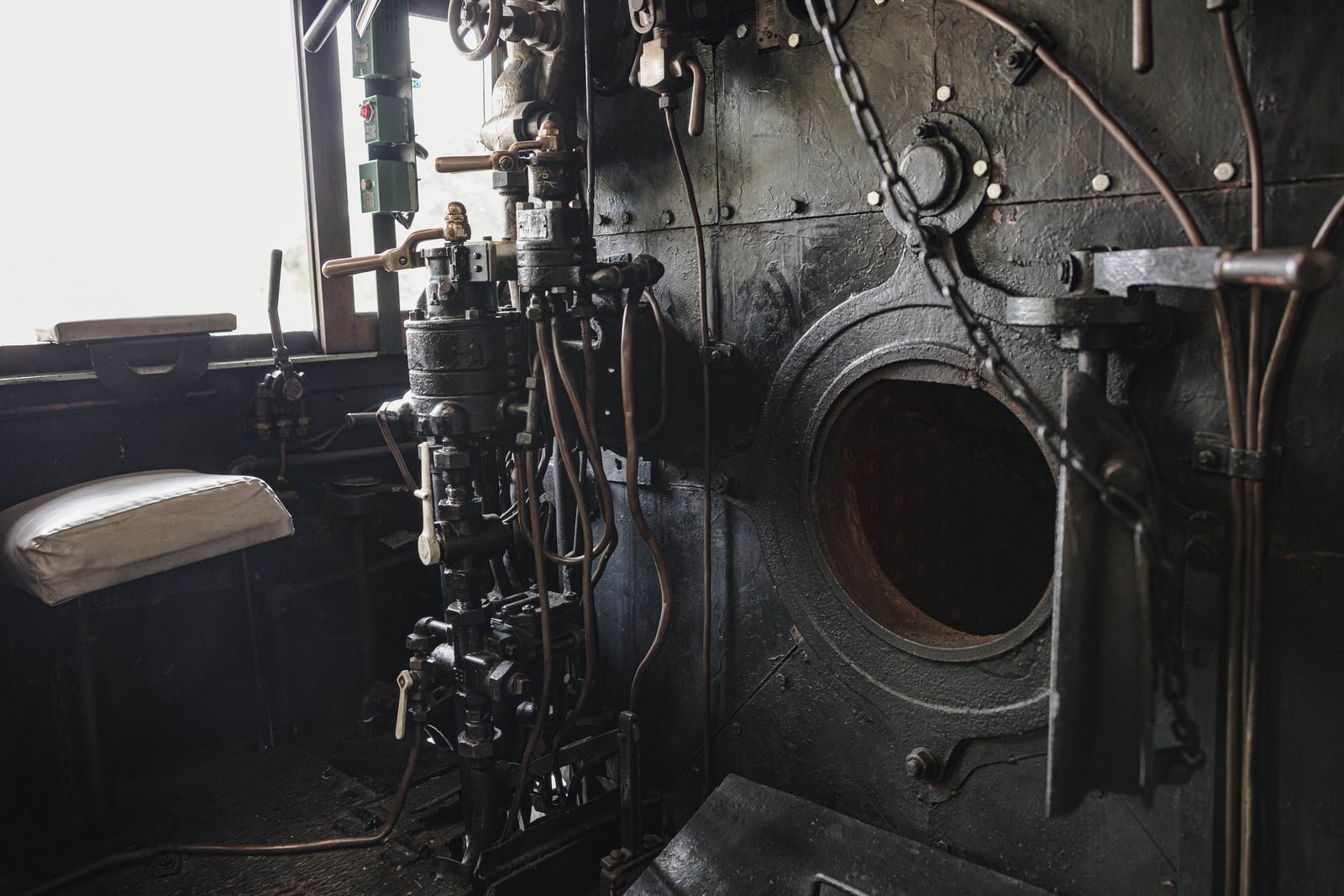 蒸気機関車の機関室内に見える開いた焚口戸と金属製のブレーキ弁ハンドル