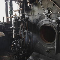 開いたままの焚口戸とブレーキ弁ハンドルが配置された蒸気機関車の機関室の写真