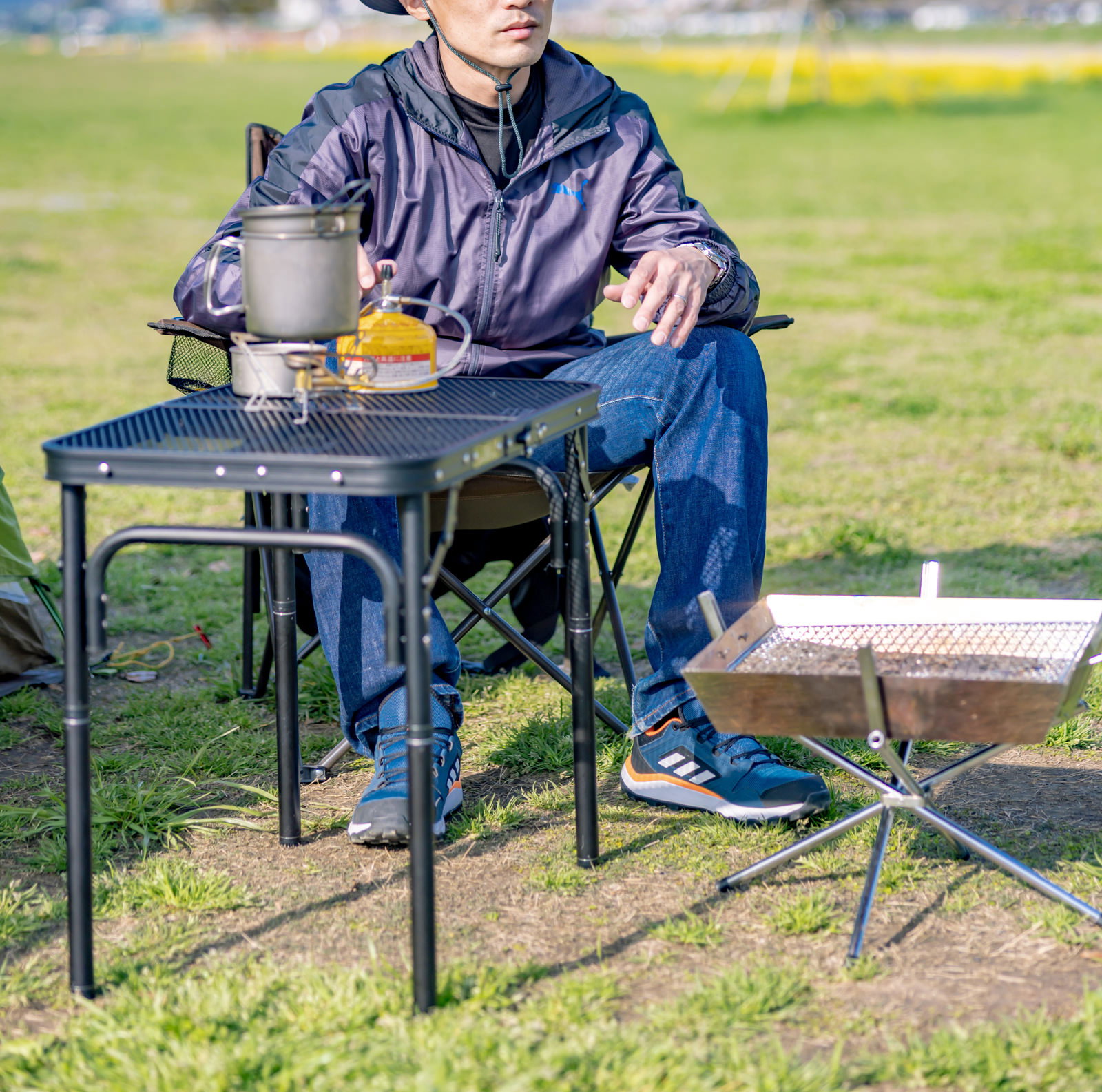 青いキャンプテーブルに座ってくつろぐ紺色ジャケットの男性