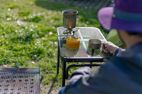 キャンプ場の焚き火台でコーヒーを淹れる男性