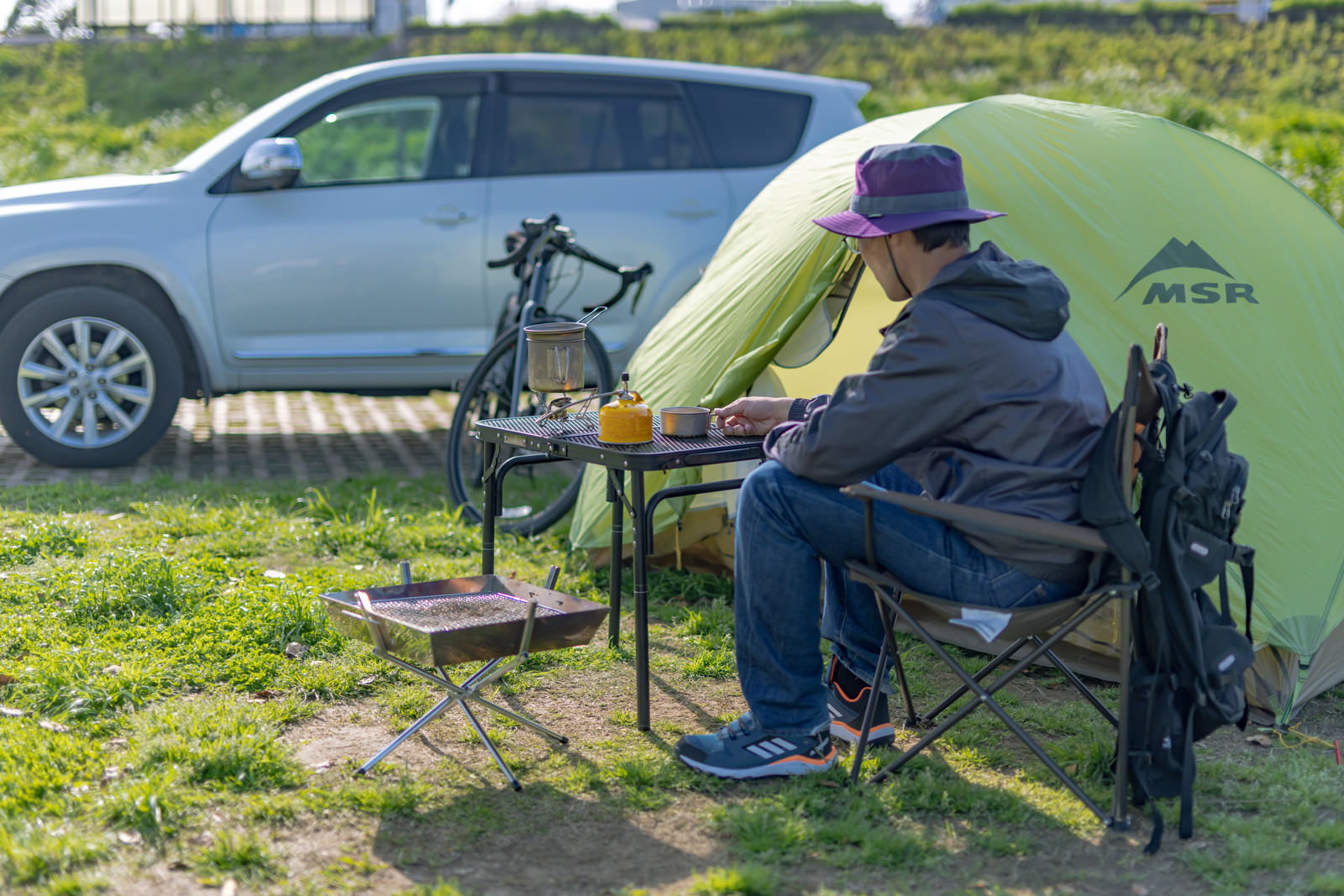 緑の芝生でテントを設営するソロキャンプの男性と車［モデル：モデルリリース］
