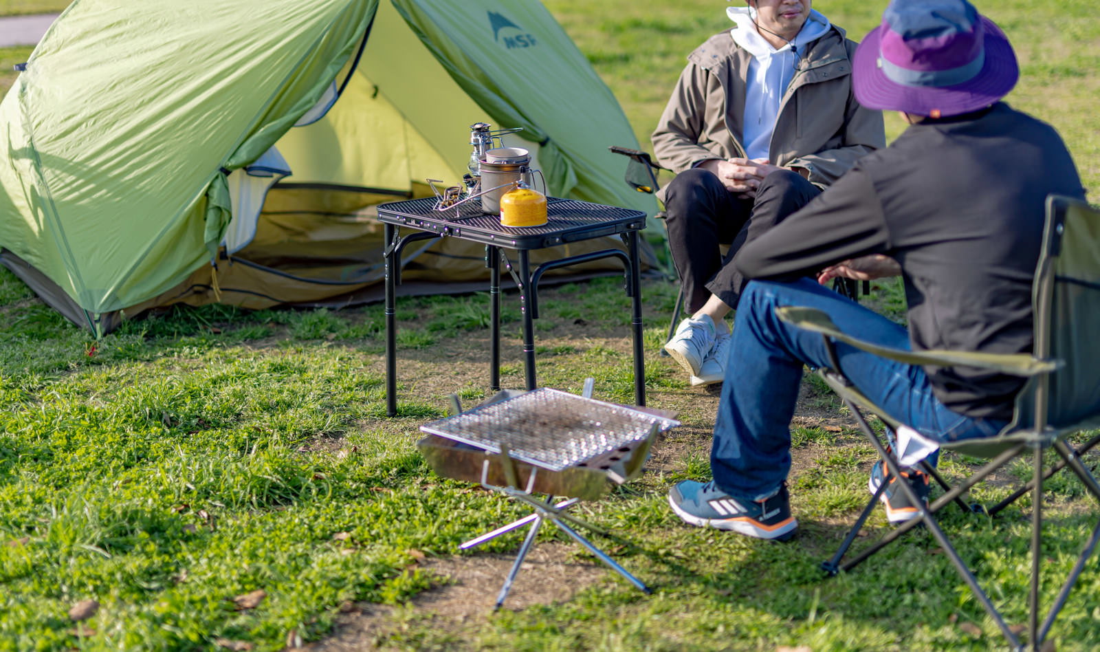 オートキャンプ場でテントを張り、焚き火台を囲んで仲間同士でBBQを楽しんでいる様子
