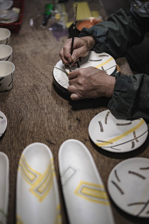 白い陶板に黄色い絵の具で丁寧に絵付けをする職人の手元